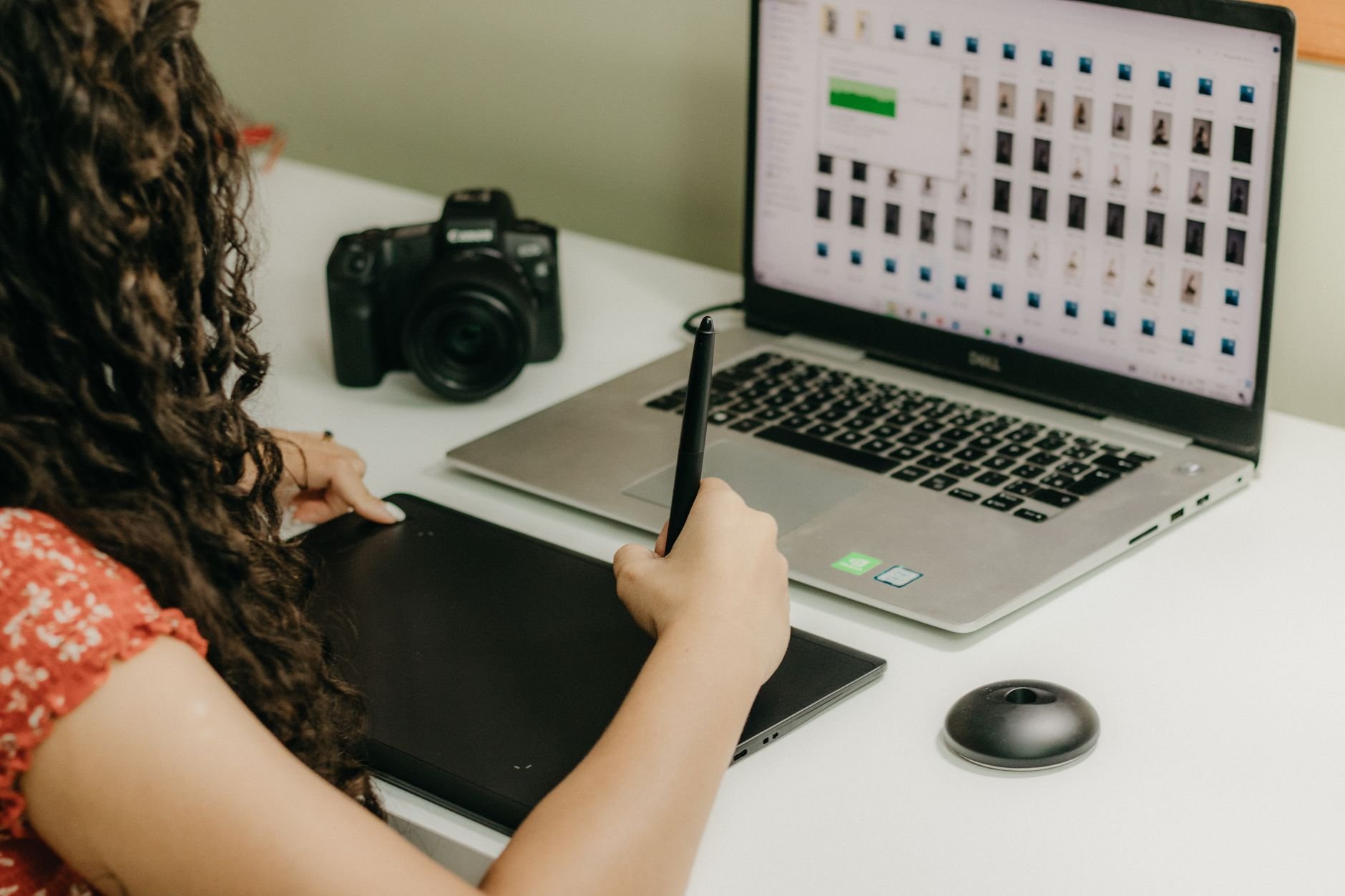 A woman using a graphics tablet and laptop, reviewing photos. Ideal for creative workspace themes.